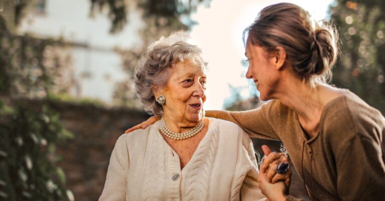 Elderly woman and adult daughter share a joyful, affectionate moment in a sunny garden.